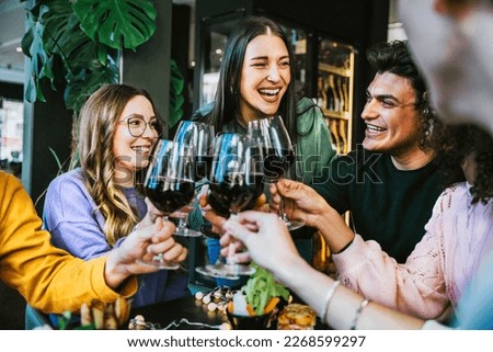 Group of friends clinking and cheers red wine glasses sitting at table bar restaurant-Young people having fun and toasting wine together enjoying happy hour at winery pub-Lifestyle concept