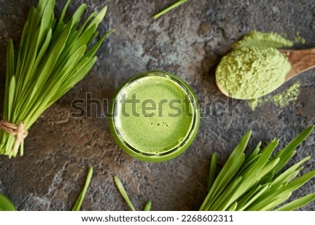 A glass of green barley grass juice with fresh homegrown blades and powder, top view Royalty-Free Stock Photo #2268602311
