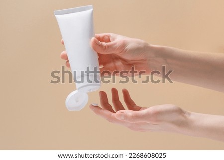 Horizontal image of female hands squeezing cream from a white blank tube. Concept of cosmetology and natural skin care product. Mockup for your design. Royalty-Free Stock Photo #2268608025