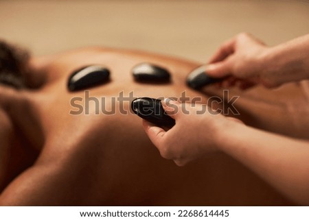 Spa therapist putting hot stones on back of young woman Royalty-Free Stock Photo #2268614445
