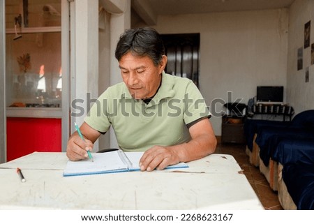Hispanic Teacher at Home - Happy Mayan Adult Writing in a Notebook - Retired Adult Budgeting at Home - Adult Learning Royalty-Free Stock Photo #2268623167