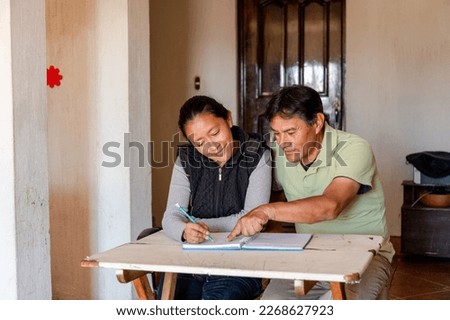 Hispanic adult couple studying together - Mayan teacher teaching senior how to write - couple budgeting at home Royalty-Free Stock Photo #2268627923