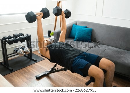 Strong fit man in his 20s with a home gym doing bench press exercises with dumbbell weights Royalty-Free Stock Photo #2268627955
