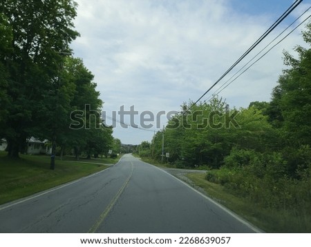 A wide open highway through a rural area under a cloudy sky on a summer day.