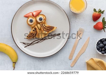 A plate of pancakes in the shape of an owl served with fruit and juice.