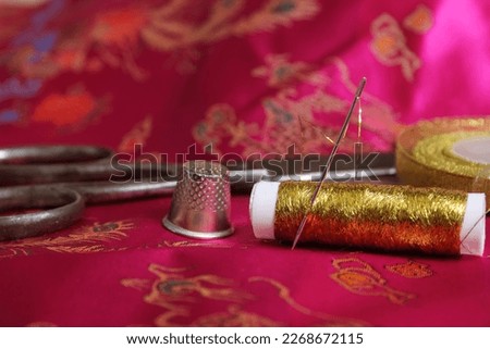 Spool of Gold Thread and Thimble on Vintage Pink Satin Fabric