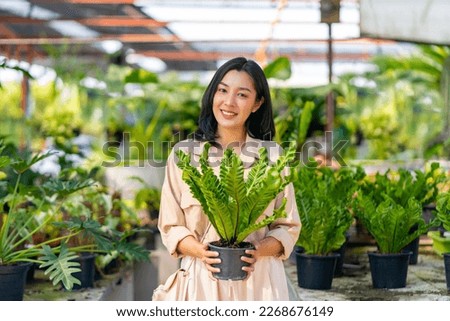 Portrait of Happy Asian woman holding potted plant in front of plant shop street market on summer vacation. Attractive woman enjoy hobbies and leisure activity growing plant and flower at home. Royalty-Free Stock Photo #2268676149