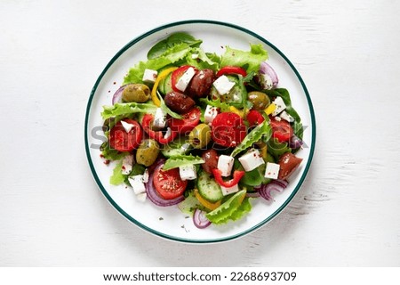 Greek salad of fresh cucumber, tomato, sweet pepper, lettuce, red onion, feta cheese and olives with olive oil on a white background. Healthy food, top view.  Royalty-Free Stock Photo #2268693709