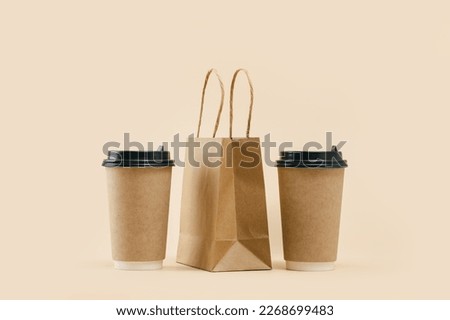 Takeaway two paper coffee cups with lunch bag on beige. Snack delivery service. Coffee to go. Grab and go or carry out beverage. Disposable mockup packaging. pair. Minimal Royalty-Free Stock Photo #2268699483
