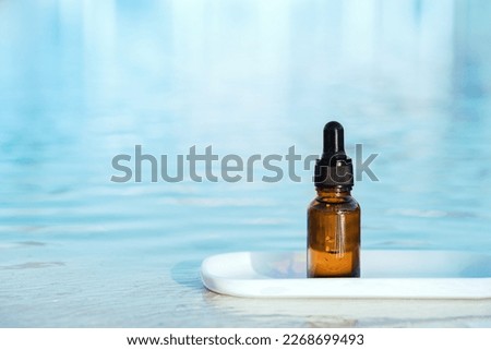 Natural medicine or essential aroma oil or beauty essence amber glass vial with dropper near blue water in sun. Face and body spa serum care concept banner. Hydration and moisturizer Royalty-Free Stock Photo #2268699493