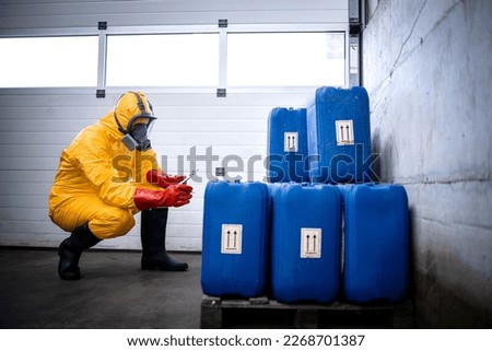 Factory worker in protection suit and gas mask checking inventory of chemicals in production plant. Royalty-Free Stock Photo #2268701387