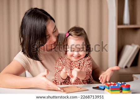 child with down syndrome with educational toys smiles, a cute girl with her mother a teacher Royalty-Free Stock Photo #2268713951