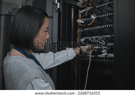 Asian woman, technician and server room for cabling, networking or system maintenance at office. Female engineer plugging wire for cable service, power or data security in admin or network management Royalty-Free Stock Photo #2268716315