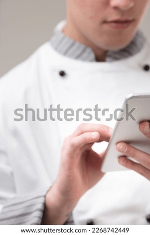 Young professional chef out of focus, in focus instead is his hand holding a tablet or cell phone with which he is managing orders, reservations, and marketing.