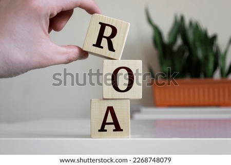 Hand holding wood cube block with 'ROA' text. ROA