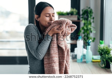 Shot of beautiful young woman holding and smelling clean clothes at home. Royalty-Free Stock Photo #2268752371