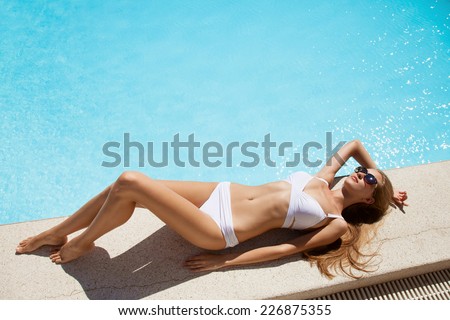 Young woman sunbathing near swimming pool.