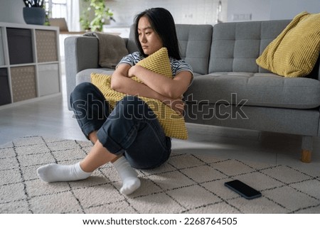 Upset korean girl feels lonely sadness suffering from bad relationship. Unhappy asian woman with pillow in hands thinks mental troubles. Depressed young female crushed by breakup sits on floor at home Royalty-Free Stock Photo #2268764505