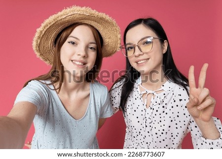 Two beautiful young women, sisters - twins on pink background