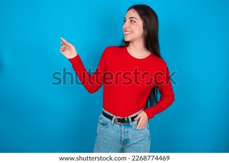 Smiling young brunette woman wearing red shirt over white studio background indicating finger empty space showing best low prices