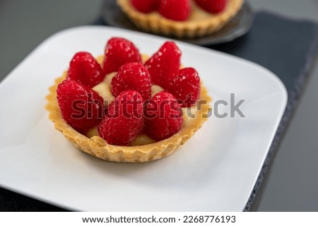Artisanal baked small tart with cream and fresh ripe red raspberry, tasty french dessert