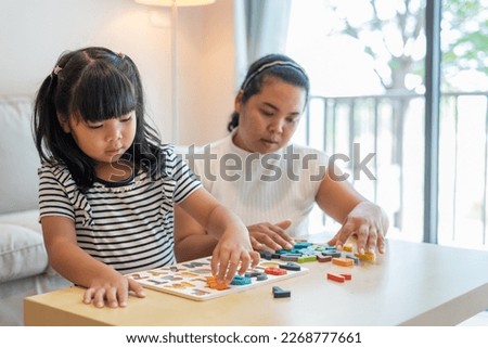 medium shot portrait of Asian girl learning English alphabet by playing jigsaw puzzle in living room at home, near her mom. Child care, family, mother and daughter concept Royalty-Free Stock Photo #2268777661