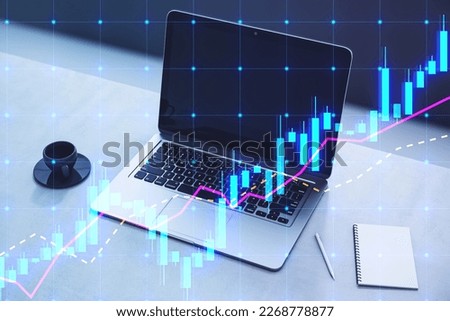 Close up of laptop on desktop with coffee cup, notepad and glowing candlestick forex chart hologram on blurry background. Trade and market concept. Double exposure
