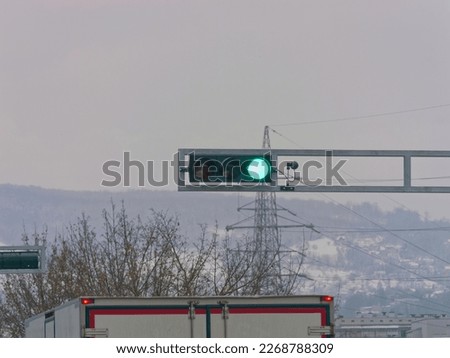 Close-up photo of a green traffic light on a metal pole with a truck below it and a cloudy sky in the background