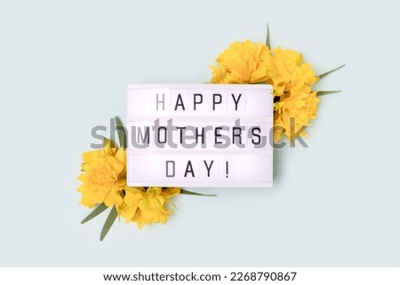 Happy Mothers Day. Lightbox with quote and frame made of yellow narcissus on a blue pastel background.