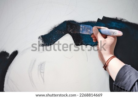 Woman artist draws with paint brush surreal girl portrait on white canvas at outdoor art painting festival, paintings art picture process. Woman in black cap paints atmospheric surreal picture