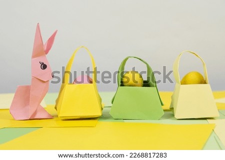 An easter bunny figurine made of paper, origami, and a baskets with eggs, place for text, happy easter.