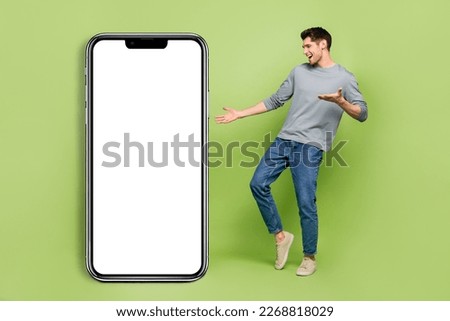 Full body photo of positive emotion male dancing around cellphone placard board isolated on green color background