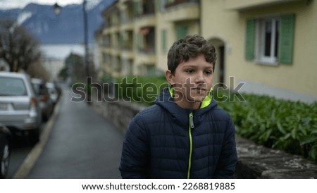 One pensive young boy walking in city street forward. Preteen male kid walks forward in urban sidewalk. Contemplative person wearing winter clothes jacket