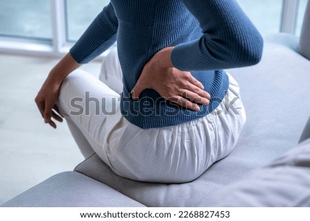 Woman suffering from back ache on the sofa. Female with back pain at home Royalty-Free Stock Photo #2268827453