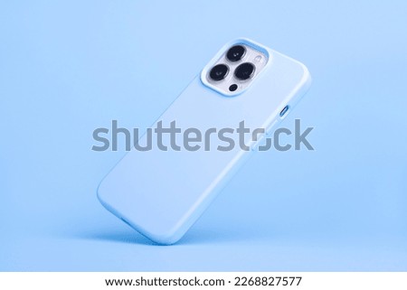 iPhone 13 and 14 Pro Max in light blue soft silicone case falls down back view, phone cover mockup in monochrome colours isolated on blue background