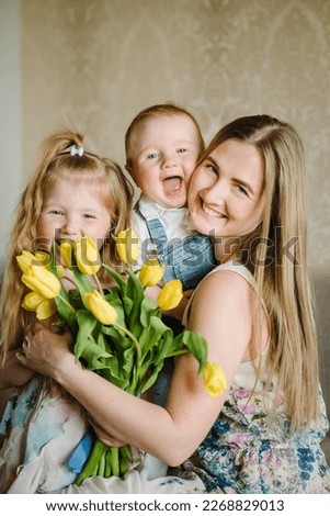 Mother's day concept. Girl and boy congratulates mother and gives a bouquet of flowers tulips at home. Mom, son and daughter smiling and hugging. Holiday greeting card for International Women's Day.