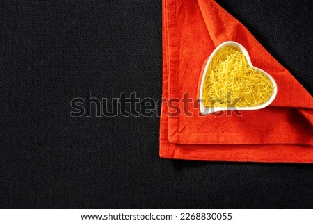 Thin vermicelli in a heart-shaped plate on a heart-shaped red napkin on a black tablecloth
