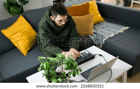 Man music producer or arranger using laptop and midi keyboard and other audio equipment to create music at home studio. Beat making and arranging audio content and composing song concept