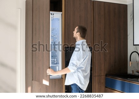 A man stands near an open refrigerator in the kitchen and studies the contents