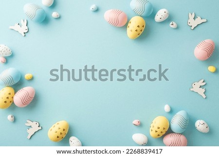 Easter decorations concept. Top view photo of colorful easter eggs and bunnies on isolated pastel blue background with copyspace in the middle