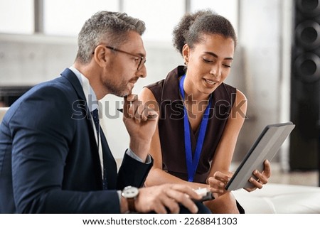 Young business woman discussing work with manager in office. Young black woman secretary showing documents on digital tablet to boss. Mature businessman and secretary working and discussing. Royalty-Free Stock Photo #2268841303
