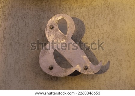 Large metal ampersand sign on concrete wall in golden light