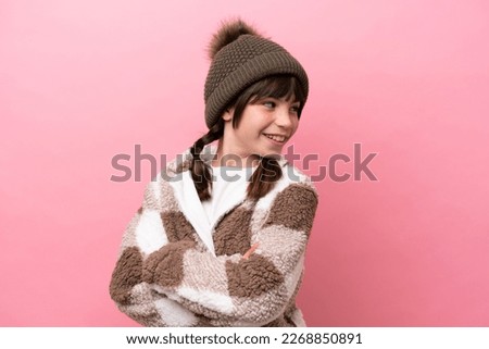 Little caucasian girl with winter jacket isolated on pink background with arms crossed and happy