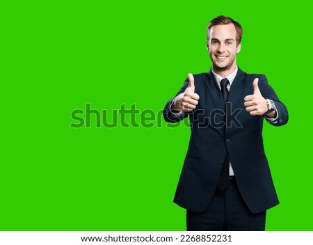 Cheerful smiling businessman in black confident suit showing two thumbs up like hand gesture, green chroma key background with copy space for ad, slogan or text. Successful business man.