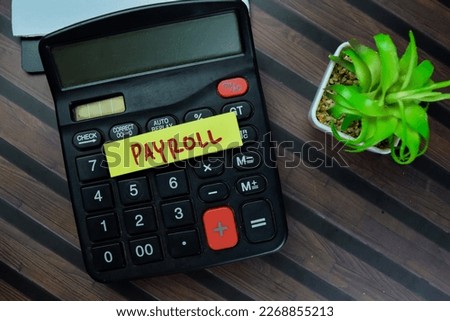 Concept of Payroll write on sticky notes with calculator isolated on Wooden Table.