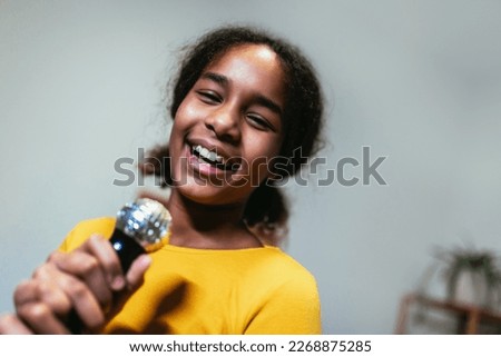Cute preteen black girl  holding microphon singing karaoke at home, recording songs for contest. Children's lifestyle concept