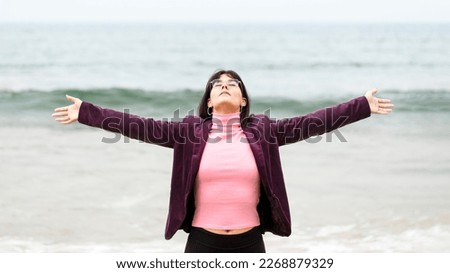 Free woman with arms outstretched breathing fresh air on the beach in front of the sea dressed in street clothes. Woman breathing fresh air relaxed with her back to the sea aware of nature  Royalty-Free Stock Photo #2268879329