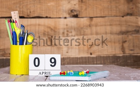 April calendar background with number  9. Stationery pens and pencils in a case on a wooden vintage background. Copy space notepad with pencils and calendar. Planner place for text.