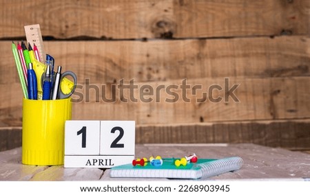 April calendar background with number  12. Stationery pens and pencils in a case on a wooden vintage background. Copy space notepad with pencils and calendar. Planner place for text.