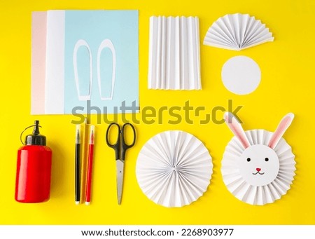 On a yellow background, the layout of the crafts.  Cute, cute Easter white rabbit made of paper.  The concept of spring, Easter holiday, children's creativity.  Flat lay, top view.